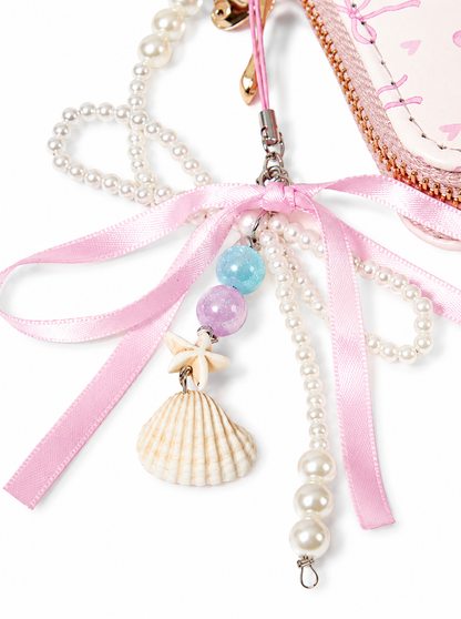 A close-up of a pastel pink and white decorative accessory with pearl strands, a pink satin ribbon, a seashell charm, pastel beads, and a small gold clasp, shown against a white background.